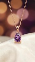Elegant rose gold chain necklace featuring a faceted amethyst teardrop pendant, displayed on white fabric with warm bokeh background. Perfect for jewelry, luxury, and fashion stock needs.