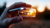 Sunset view through eyeglass lens held up against warm evening sky, capturing reflection of house silhouette in creative perspective photography composition.