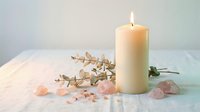 Lit candle with eucalyptus branch and rose quartz crystals on white surface creating peaceful spa atmosphere for meditation and wellness rituals.