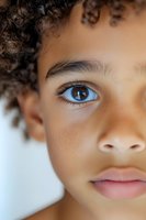 Close up portrait of young mixed race child with bright blue eyes, curly dark hair, and soft natural skin tone against light background.