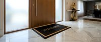 Welcome doormat with gold lettering on marble floor near wooden entrance door in modern luxury home interior.