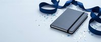 Gray notebook with elastic band surrounded by navy blue ribbon and silver confetti on white background for celebration and gift concepts.