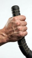 Male hand gripping black tactical flashlight with textured handle against white background for security and emergency preparedness concepts.