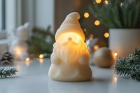 Illuminated ceramic gnome figurine with warm LED light creating cozy Christmas atmosphere among pine branches and fairy lights on white surface.
