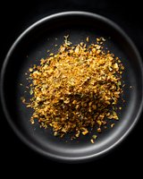 Golden crispy breadcrumbs scattered on black ceramic plate captured from above with dramatic lighting, creating contrast between bright crumbs and dark background.