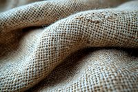 Natural burlap fabric with textured weave pattern in beige and brown tones, macro close-up showing detailed fiber structure and soft folds.