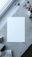Blank white paper sheet mockup on concrete surface with eucalyptus branch and natural window light for branding presentation and stationery design.