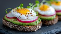 Open-faced sandwich with mashed avocado, sliced radish, poached egg and microgreens on seeded bread, served on dark stone surface. Healthy breakfast concept.