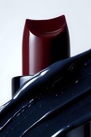 Deep burgundy lipstick with glossy black liquid splash creating dramatic contrast against white background, macro cosmetic photography for beauty advertising.