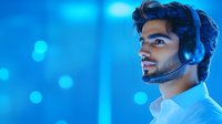 Young Middle Eastern man with beard wearing wireless headphones in profile view against blue bokeh background, expressing focus and concentration while listening.