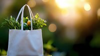 Fresh organic vegetables and greens in white eco-friendly reusable shopping bag against blurred natural bokeh background at sunset. Sustainable lifestyle concept.