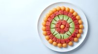 Colorful fruit platter arranged in circular pattern with melon balls, watermelon and cucumber slices on white plate, healthy snacking and party appetizer.