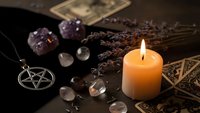 Mystical witchcraft altar with burning candle, pentagram pendant, amethyst crystals, dried lavender herbs and tarot cards for spiritual rituals and magic practices.