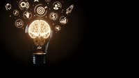 Glowing light bulb with brain filament surrounded by business icons on dark background representing innovation, creativity and entrepreneurship concepts.