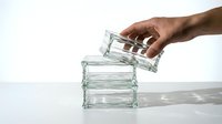 Hand stacking clear glass containers on white surface, minimalist kitchen organization and storage concept for modern home design applications.