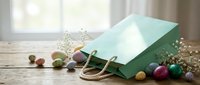 Green paper shopping bag with handles on rustic wooden table surrounded by colorful Easter eggs and spring flowers for holiday retail and gift concepts.