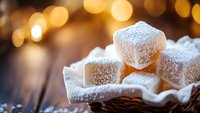 Homemade marshmallow cubes dusted with powdered sugar in rustic basket against warm bokeh lights background, macro food photography for confectionery and desserts.