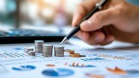 Stacked coins on financial charts with hand analyzing data, representing business growth, investment strategy and financial planning concept.