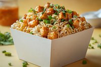 Asian noodles topped with glazed chicken pieces in sweet and spicy sauce, garnished with fresh chopped green onions, served in white takeout box.