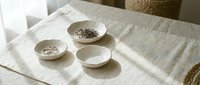 Neutral ceramic bowls with seeds and grains arranged on linen fabric, showcasing natural textures and minimalist tableware styling for home decor and culinary projects.