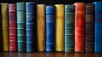 Row of vintage hardcover books spines on dark background showing colorful collection in blue, red, yellow and green bindings, arranged neatly on shelf.