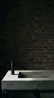 Modern concrete sink with black matte faucet against dark brick wall. Industrial bathroom or kitchen fixture for contemporary interior design and home renovation projects.