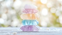 Colorful healing crystals stacked in zen balance on rustic wooden surface against soft bokeh background, creating peaceful spiritual atmosphere.