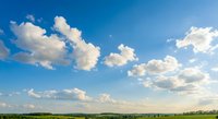 Dramatic blue sky with fluffy white clouds over green countryside landscape on sunny day for nature backgrounds and outdoor advertising campaigns.