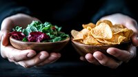 Hands holding wooden bowls with fresh salad and crispy chips offering healthy versus unhealthy food choice concept for nutrition and diet decisions.