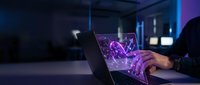 Businessman holding transparent laptop displaying glowing purple digital network hologram, futuristic technology concept for innovation and digital transformation in modern workspace.
