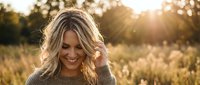 Young blonde woman laughing with hand in hair during golden hour sunset in natural outdoor setting for lifestyle and wellness content.