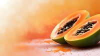 Fresh ripe papaya fruit cut in half showing black seeds on orange gradient background with copy space for healthy tropical nutrition concepts.