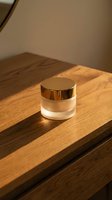 Luxury cosmetic jar with golden cap on wooden surface in warm natural lighting for skincare and beauty product packaging design.