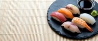 Assorted nigiri sushi with salmon, tuna, shrimp and scallop on black slate plate with bamboo placemat, Japanese cuisine food styling.