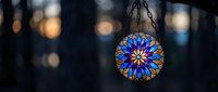 Ornate stained glass pendant lamp with intricate blue floral mandala pattern hanging against blurred bokeh lights creating warm atmospheric lighting.