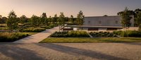 Modern minimalist house with landscaped garden and paved driveway at sunset. Contemporary residential architecture with clean lines and natural surroundings.