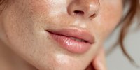 Close-up of young Caucasian woman's face with natural freckles and full glossy lips, showcasing natural beauty and skin texture.