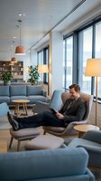 Professional businessman relaxing in modern office lounge area with tablet, contemporary furniture and large windows creating comfortable workspace atmosphere.