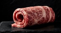 Premium marbled beef roll on dark slate surface showcasing rich fat distribution and texture for culinary presentations and gourmet cooking concepts.