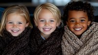 Diverse children wrapped in cozy knit blankets showing genuine happy smiles, representing friendship, warmth and togetherness in winter season.