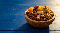 Mixed nuts and dried fruits in wooden bowl on rustic blue table for healthy snacking and cooking ingredients.