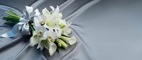 Elegant white lily wedding bouquet with silver ribbon on soft gray fabric background for bridal ceremonies and romantic celebrations.