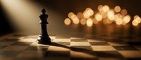 Black chess king piece standing alone on wooden chessboard with warm golden bokeh lights creating dramatic atmosphere for strategic thinking concepts.