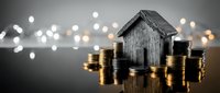 Wooden house model surrounded by stacks of golden coins with bokeh lights background representing real estate investment and property savings concept.