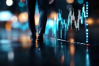 Business person walking past digital stock market chart display with glowing blue data visualization and bokeh lights on reflective floor surface.