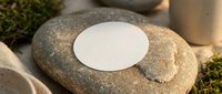 Blank white circular label mockup on natural stone surface with moss accents for branding and product presentation in organic spa setting.
