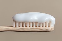 Wooden bamboo toothbrush with white toothpaste on bristles against neutral beige background, promoting eco-friendly dental care.