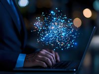 Glowing blue digital particles burst above laptop keyboard while business professional works in dark office, representing digital transformation and innovation.