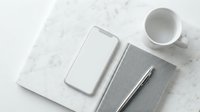 Minimalist workspace with smartphone, notebook, pen and coffee cup on marble surface for business and productivity concepts.