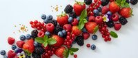 Fresh mixed berries including strawberries, blueberries, raspberries, blackberries and red currants with mint leaves scattered on white background.
